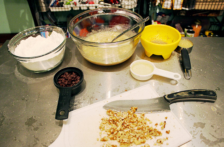 Assembly of all ingredients: dry ingredients (mixed), macerated bananas, flax egg, applesauce egg, liquefied vegetable shortening, walnuts, and dark chocolate chips